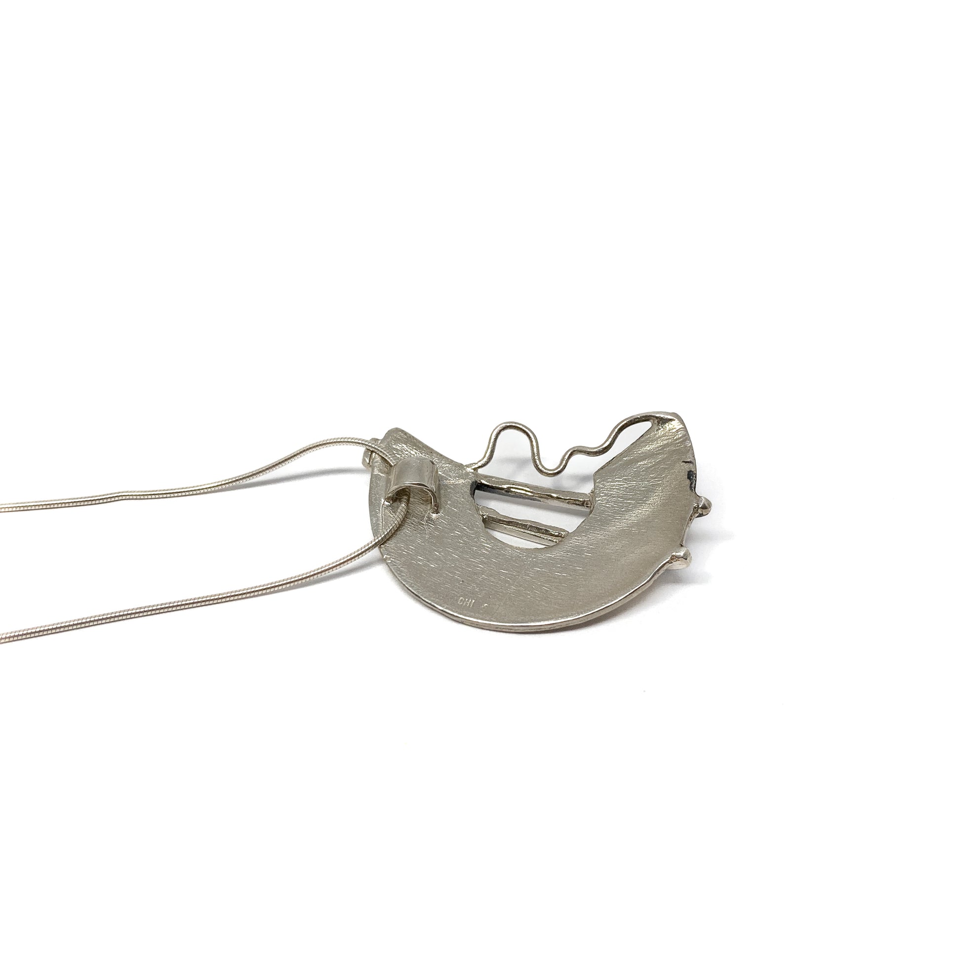 A silver pendant necklace with a semi-circular design and abstract lines. The pendant hangs from a delicate silver chain.