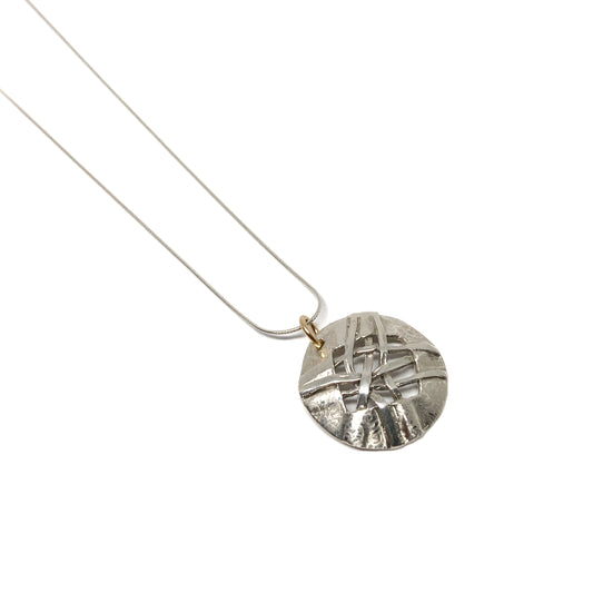 A silver pendant necklace with a circular disc pendant featuring a woven design. The pendant hangs from a delicate silver chain.