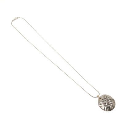 A silver pendant necklace with a circular disc pendant featuring a woven design. The pendant hangs from a delicate silver chain.