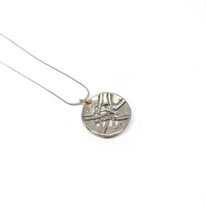A silver pendant necklace with a circular disc pendant featuring a woven design. The pendant hangs from a delicate silver chain.