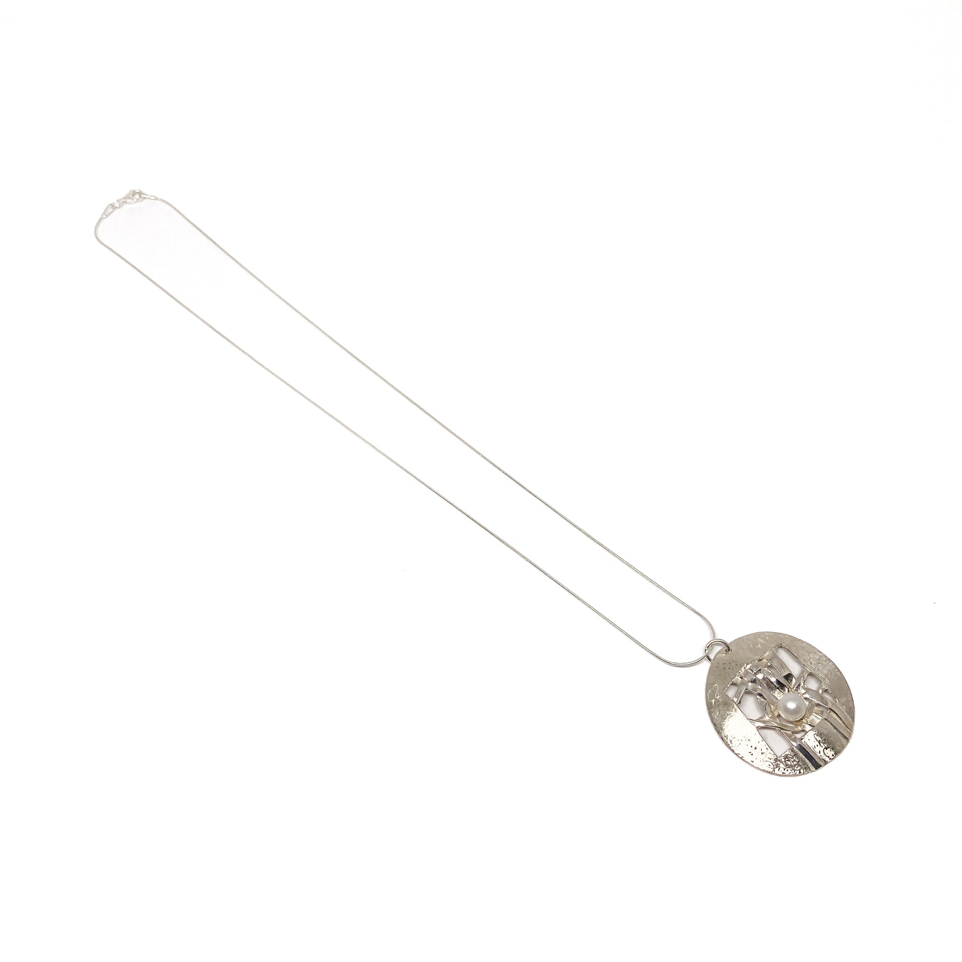 A silver pendant necklace with a circular disc pendant featuring a woven design and a pearl accent. The pendant hangs from a delicate silver chain.