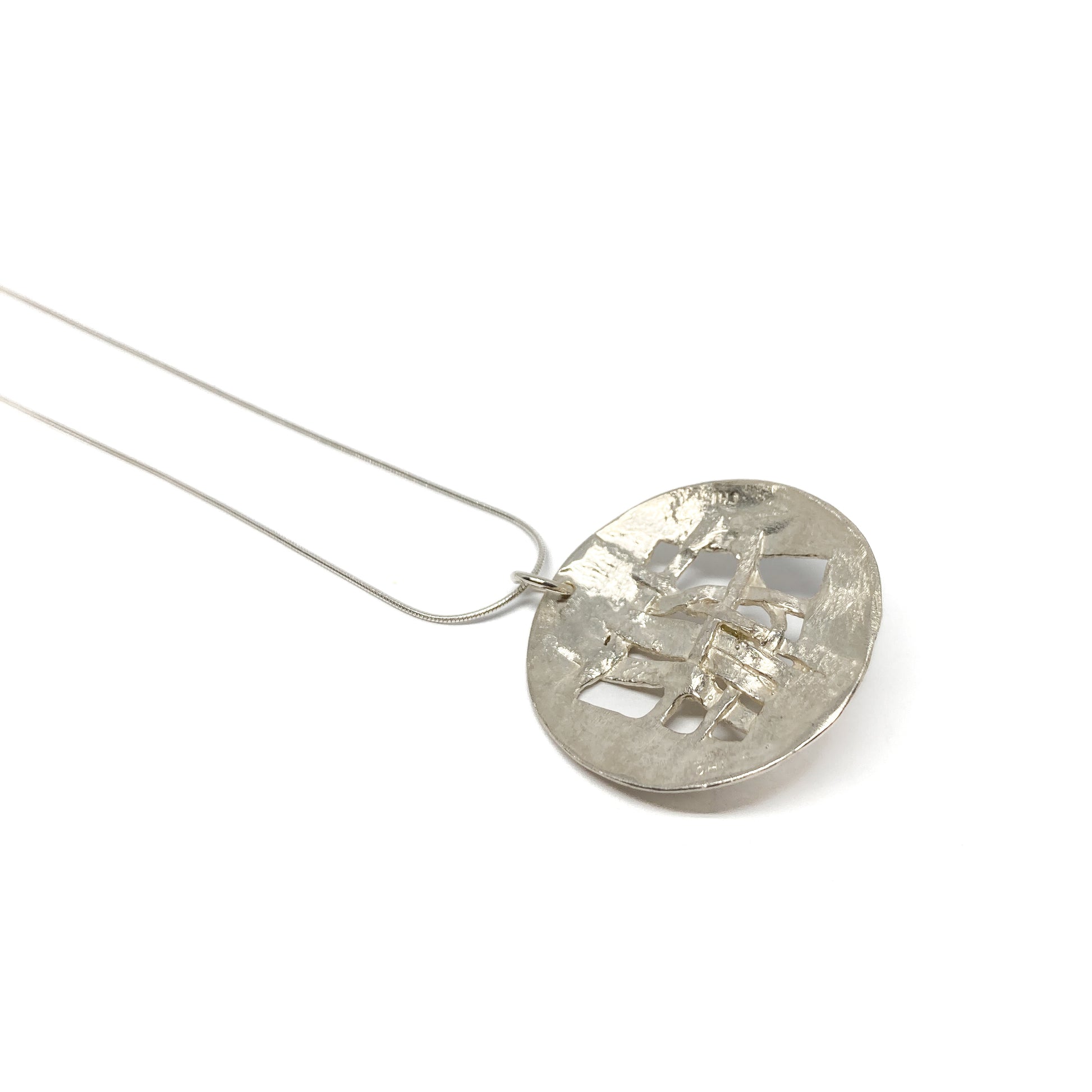 A silver pendant necklace with a circular disc pendant featuring a geometric cut-out design. The pendant hangs from a delicate silver chain.