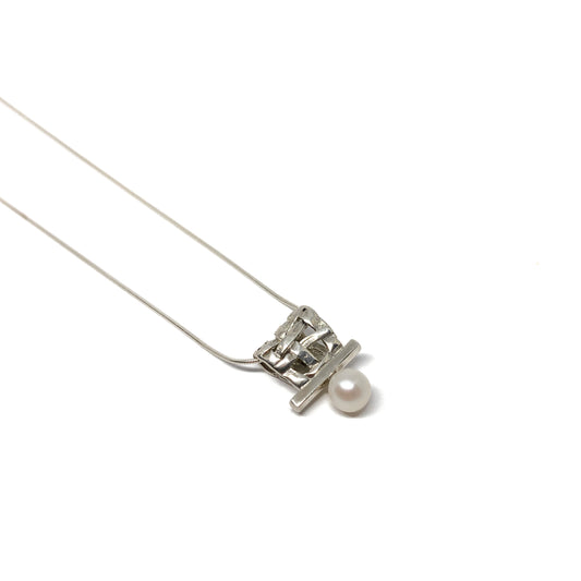 A silver pendant necklace with a square woven design and a single pearl accent. The pendant hangs from a delicate silver chain.