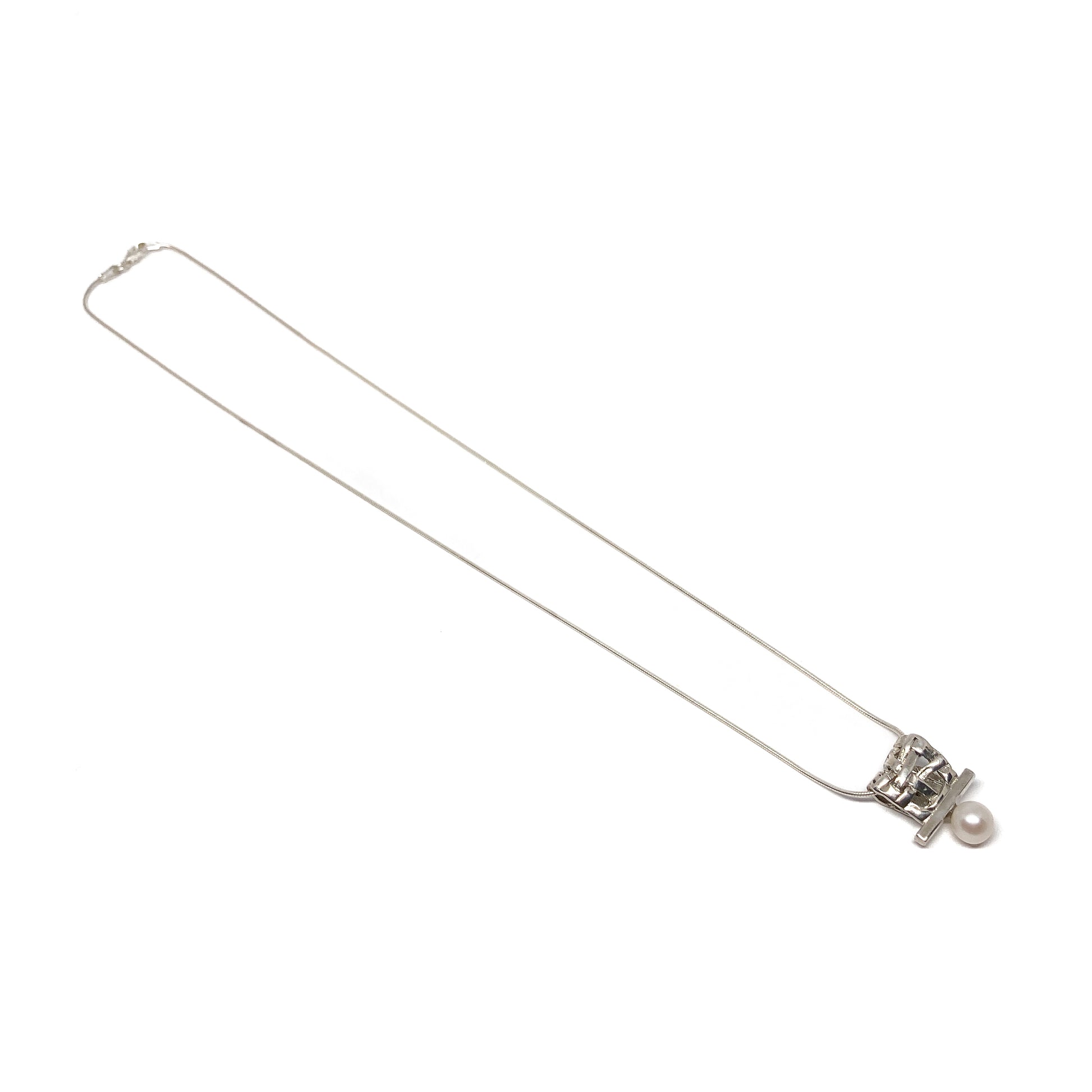 A silver pendant necklace with a square woven design and a single pearl accent. The pendant hangs from a delicate silver chain.