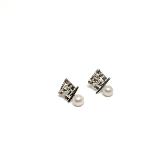 A pair of silver stud earrings with a square woven design and a single pearl accent on each. The earrings have a post back closure.