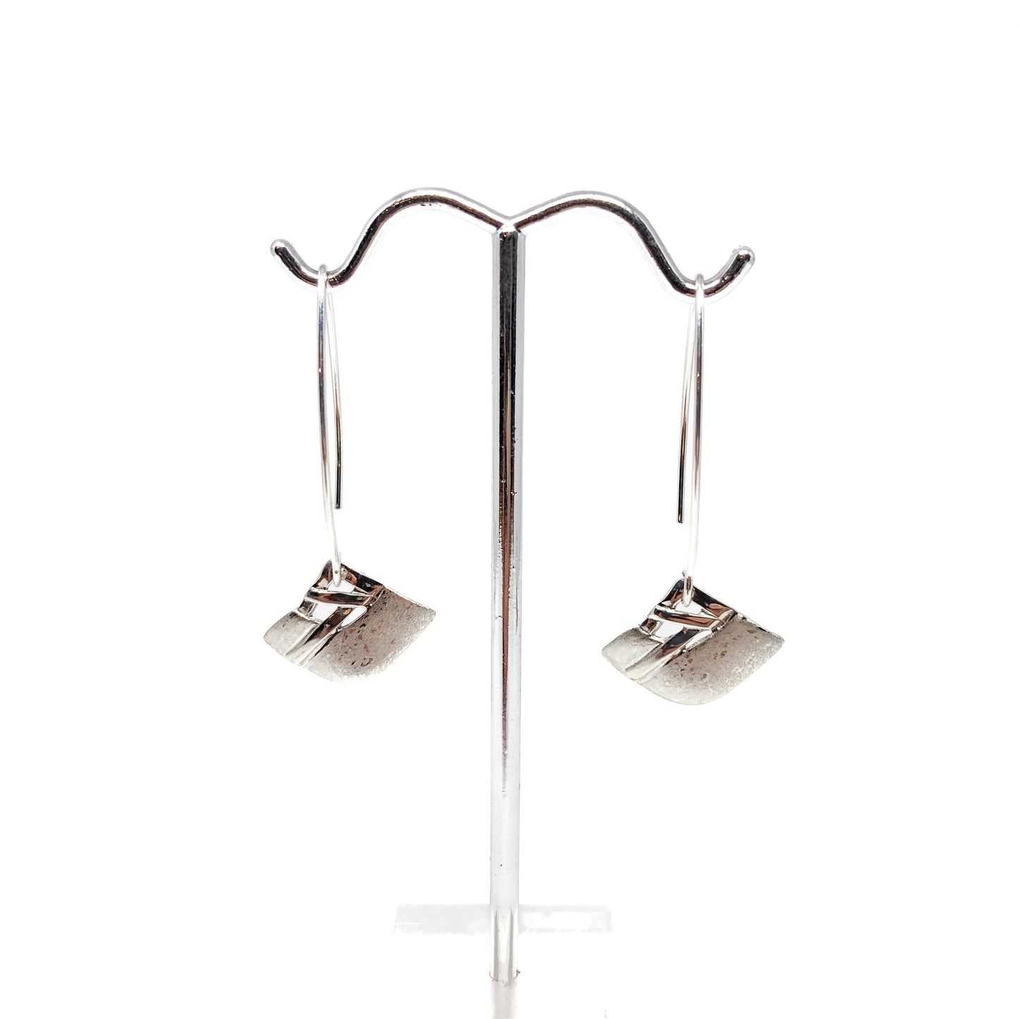 A pair of silver dangle earrings with a square woven design, displayed on a metal earring stand. The earrings have long, curved hook closures.