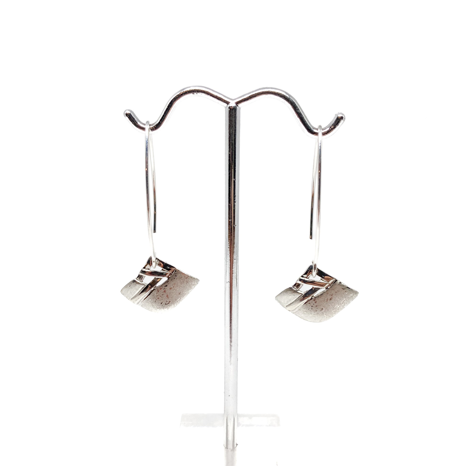 A pair of silver dangle earrings with a square woven design, displayed on a metal earring stand. The earrings have long, curved hook closures.