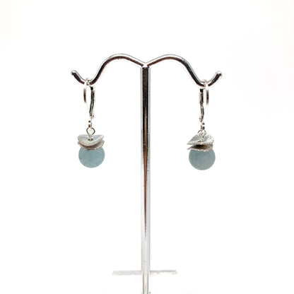 A pair of silver lever-back earrings with light blue beads and a textured, petal-like design, displayed on a metal earring stand. The earrings have a secure lever closure.