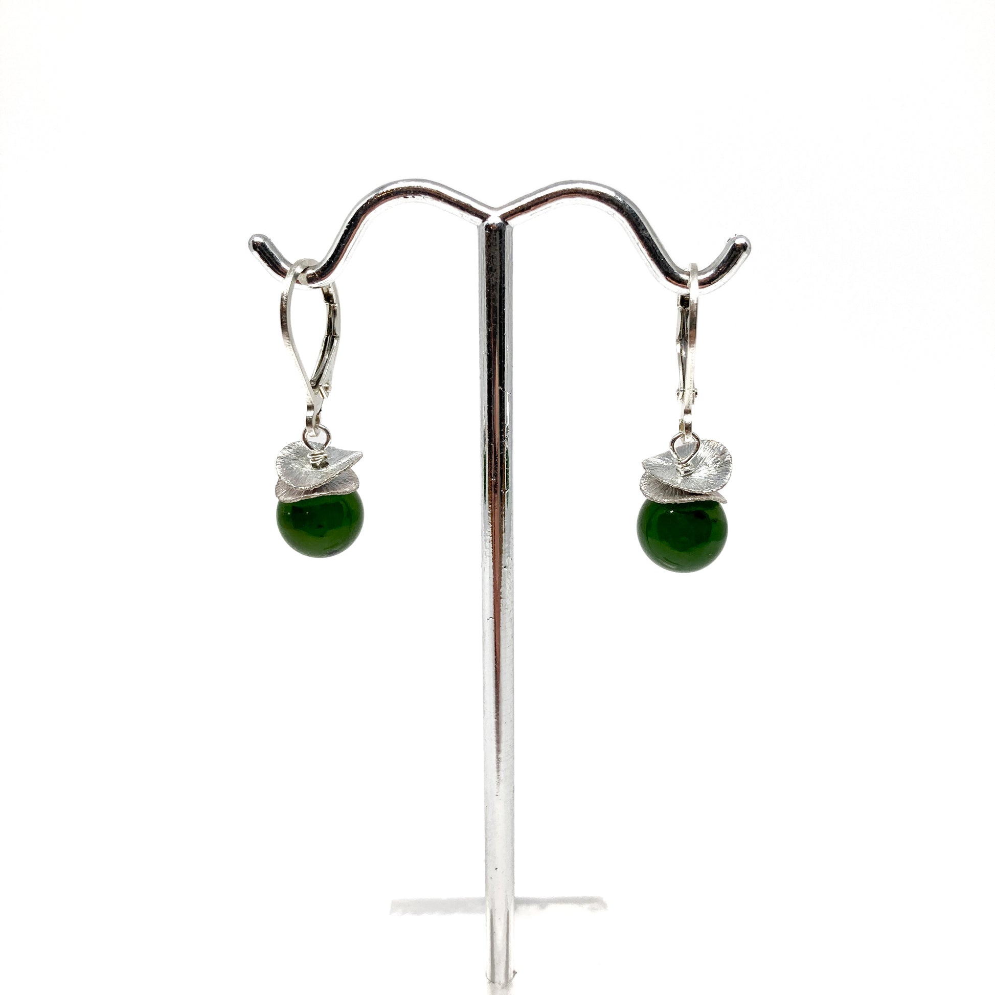 A pair of silver lever-back earrings with dark green beads and a textured, petal-like design, displayed on a metal earring stand. The earrings have a secure lever closure.