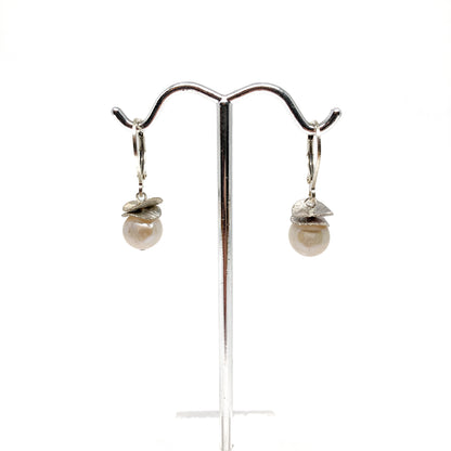 A pair of silver lever-back earrings with pearl beads and a textured, petal-like design, displayed on a metal earring stand. The earrings have a secure lever closure.