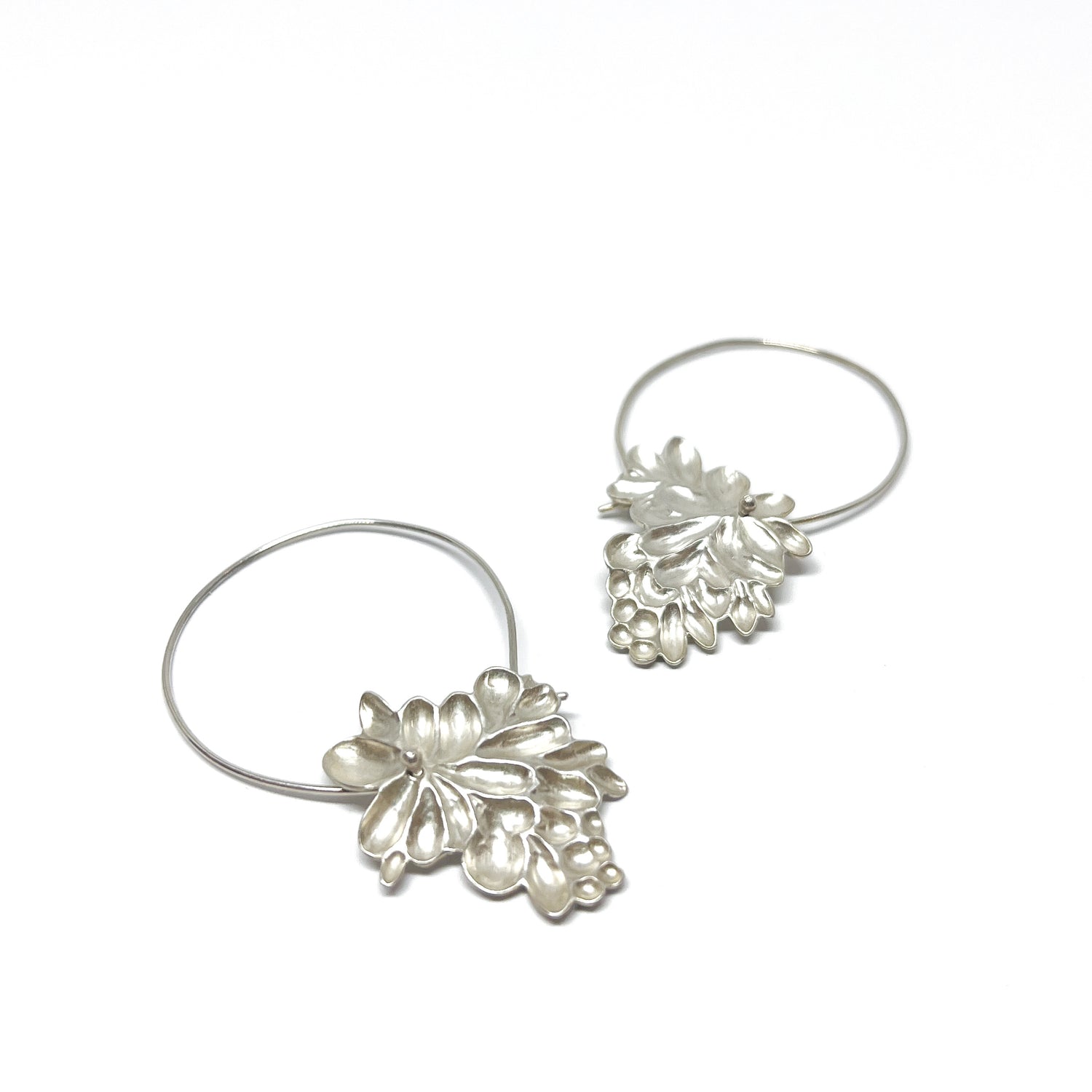 A pair of silver hoop earrings featuring detailed, textured pendants resembling clusters of stylized flowers or berries.