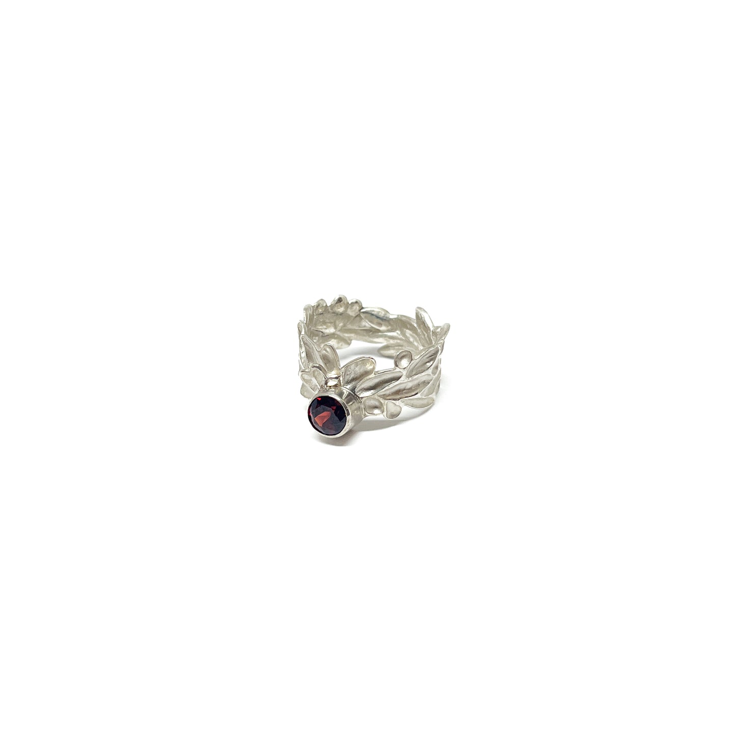 A sterling silver ring with a textured, abstract leaf or floral design and a single, round dark red garnet gemstone.