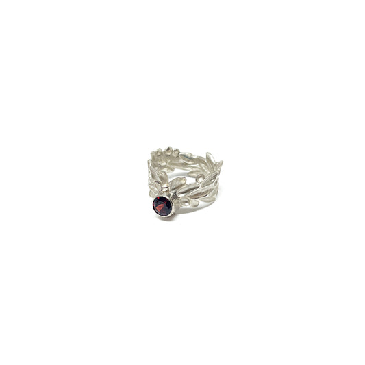 A sterling silver ring with a textured, abstract leaf or floral design and a single, round dark red garnet gemstone.