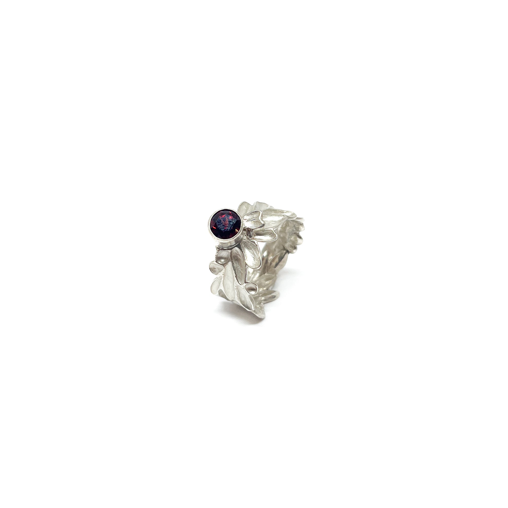 A textured sterling silver ring with abstract, organic shapes and a single, round deep red garnet gemstone setting.