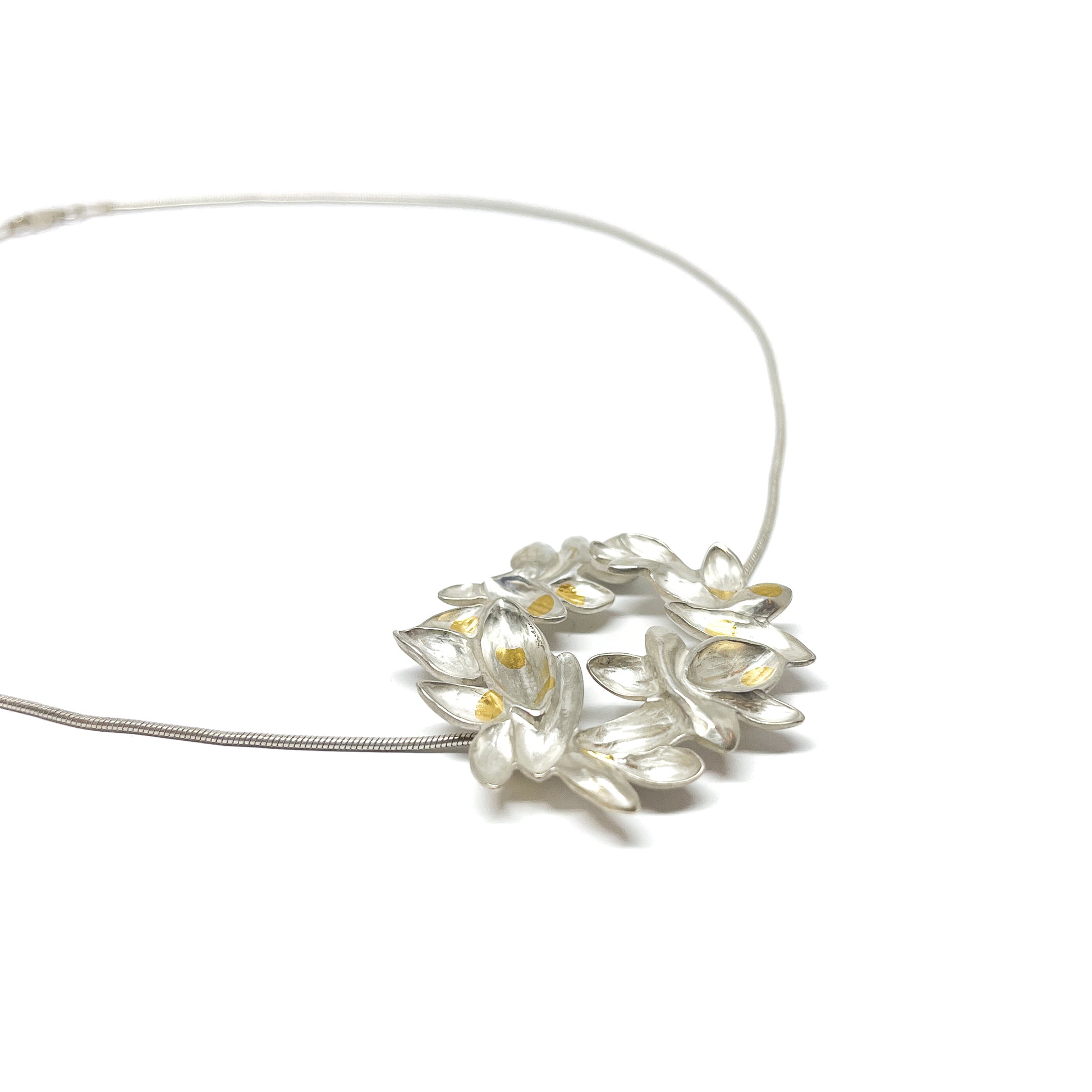 A delicate silver necklace with a circular pendant of textured, abstract floral forms highlighted with Keum-Boo gold.