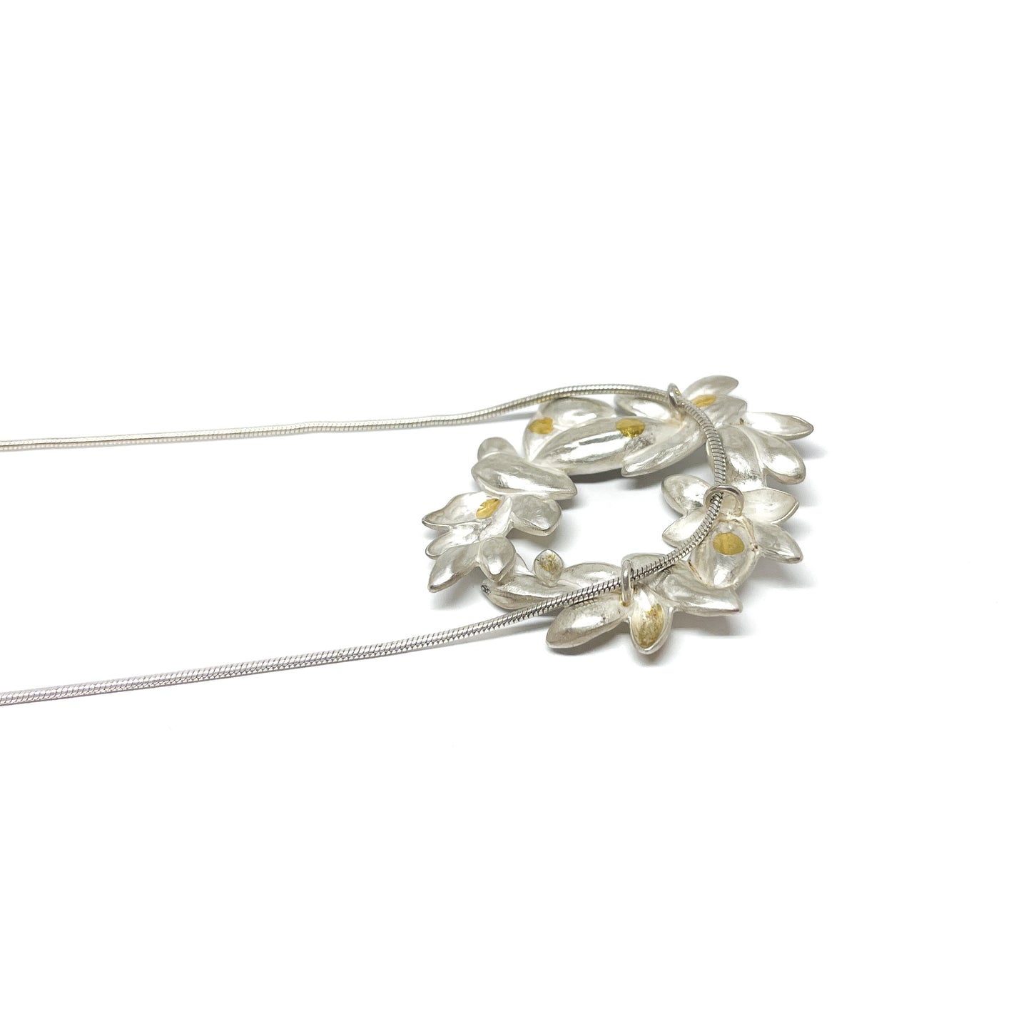 A silver snake chain necklace featuring a circular pendant of textured, abstract floral shapes with small Keum-Boo gold details.