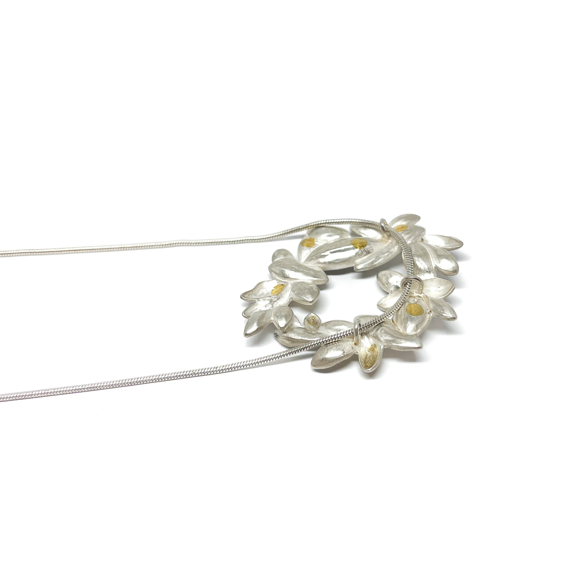 A silver snake chain necklace featuring a circular pendant of textured, abstract floral shapes with small Keum-Boo gold details.