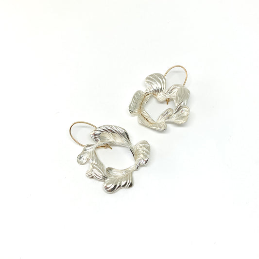 A pair of handmade silver drop earrings with textured, abstract floral or leaf-like shapes and gold-toned hooks.