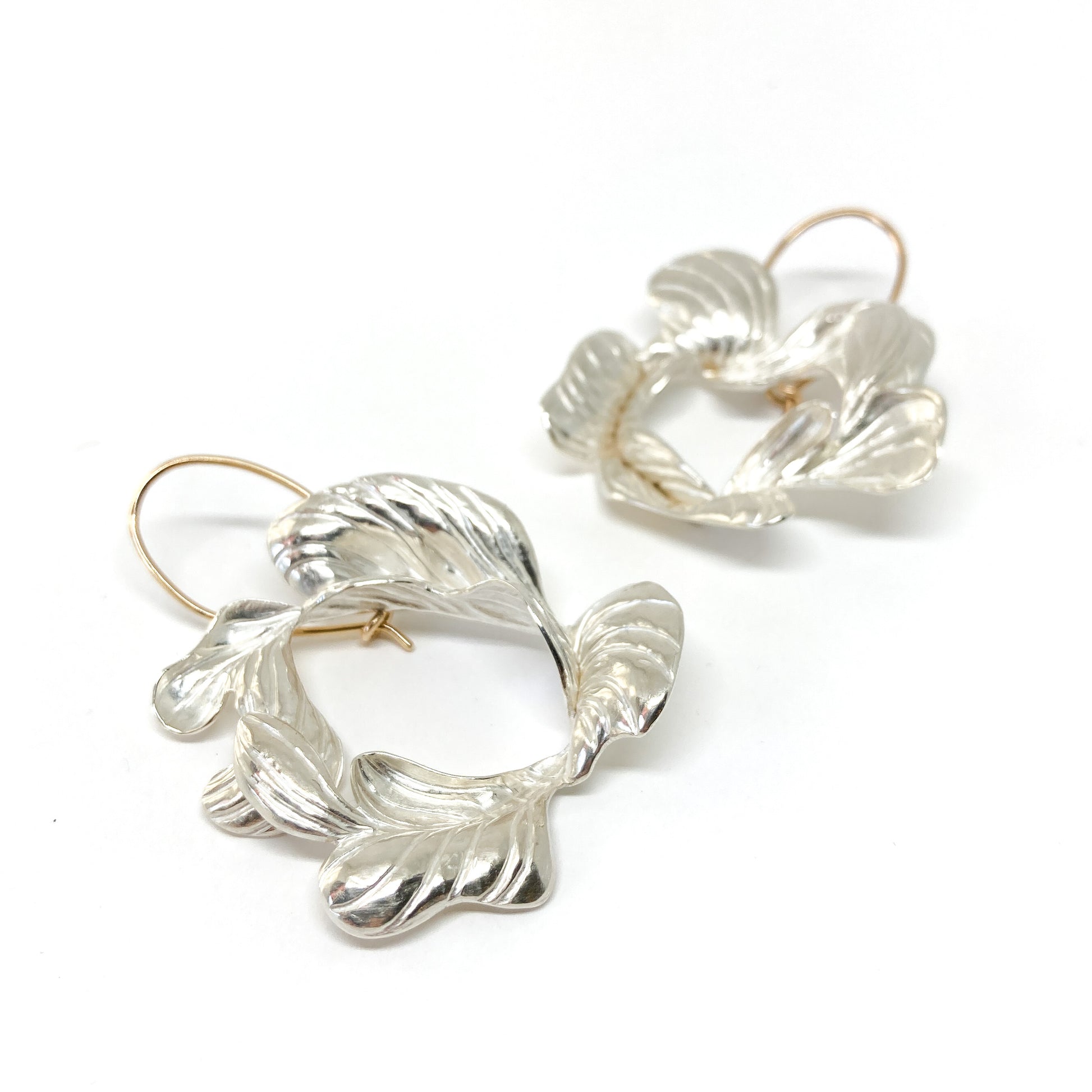 A pair of Closeness Earrings by Erin Christensen: silver with textured, abstract floral or leaf-like shapes and gold-toned hooks.