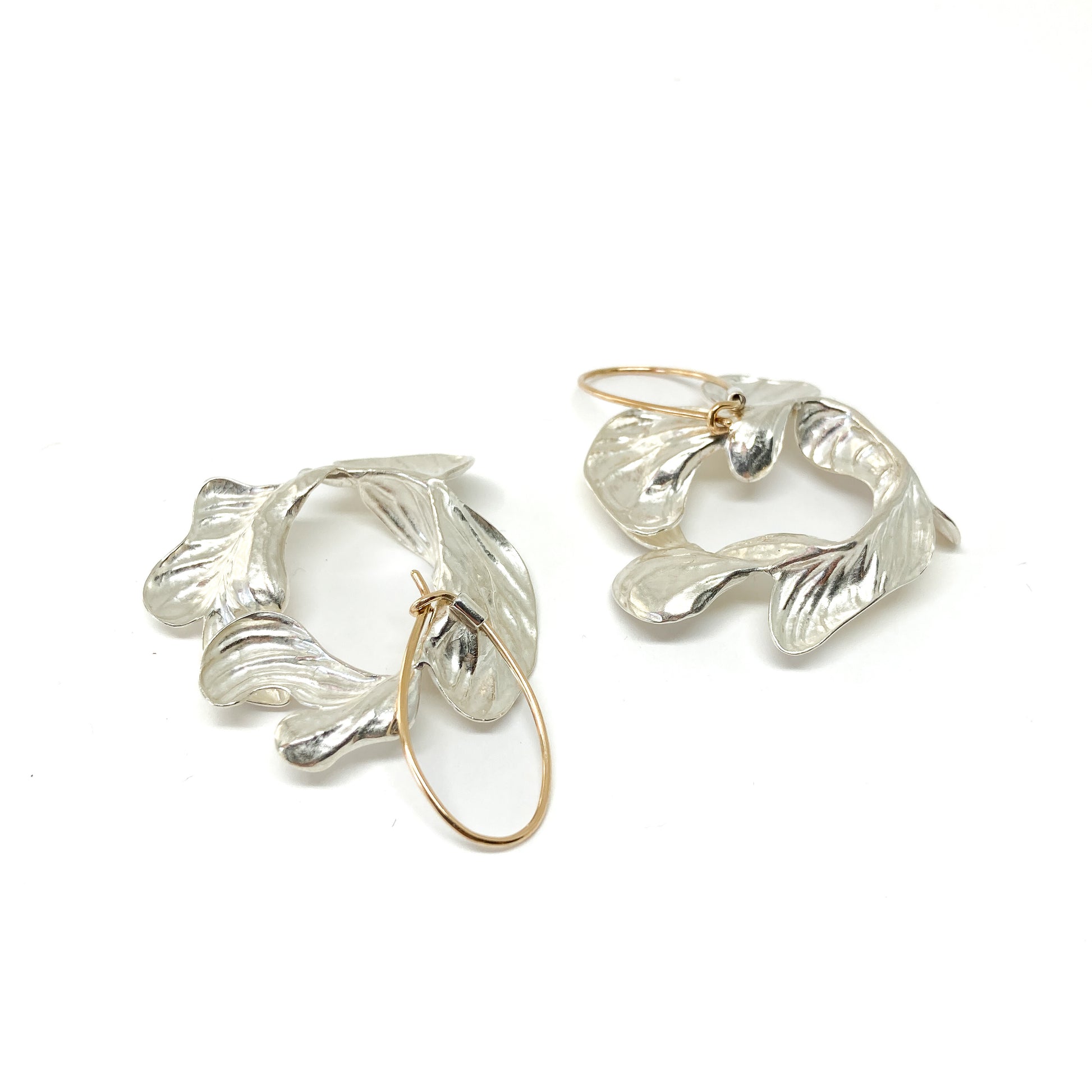 A pair of silver drop earrings with textured, abstract floral or leaf-like shapes and gold-toned hoops.