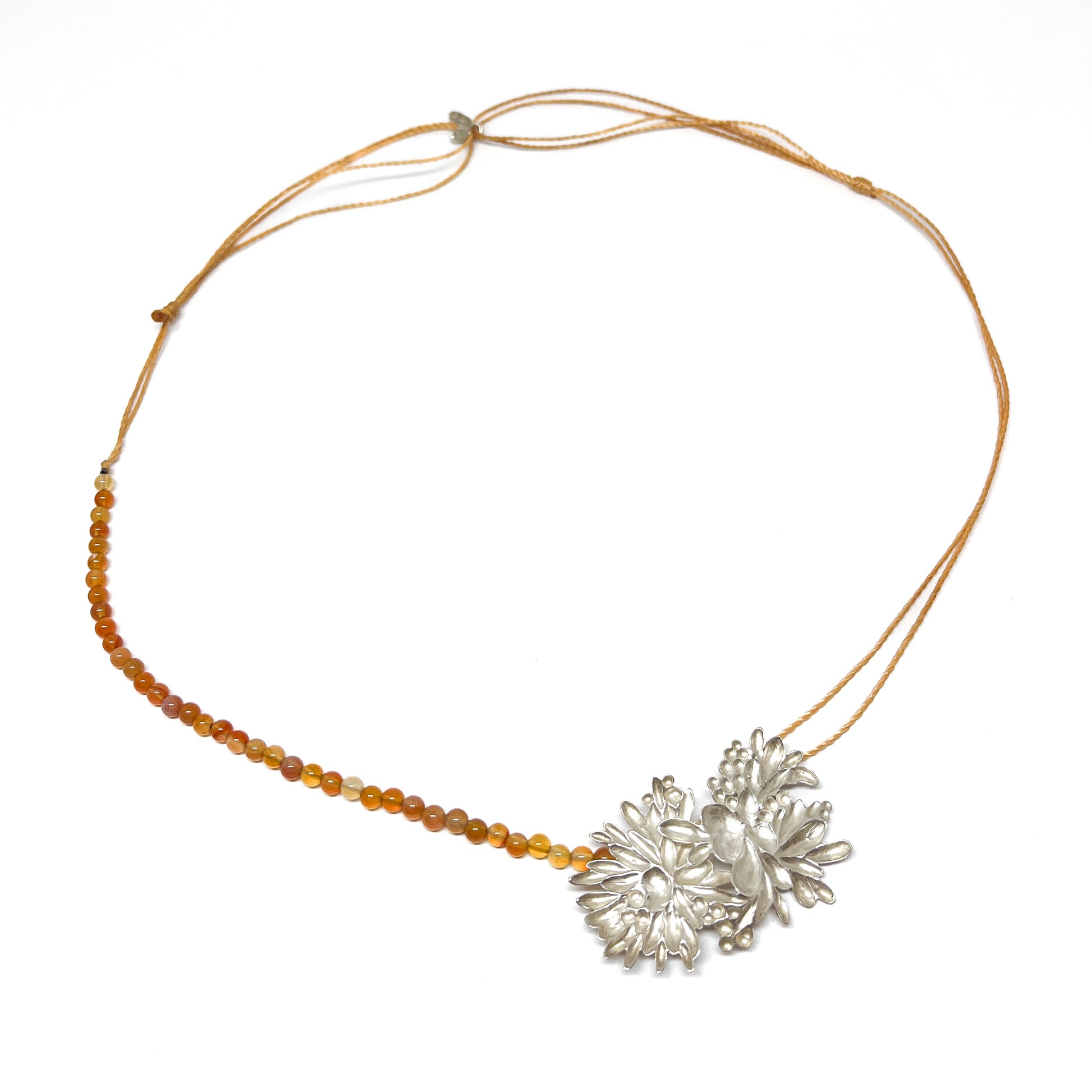 A necklace featuring a textured silver floral pendant connected to a string of small orange beads and a thin adjustable cord.