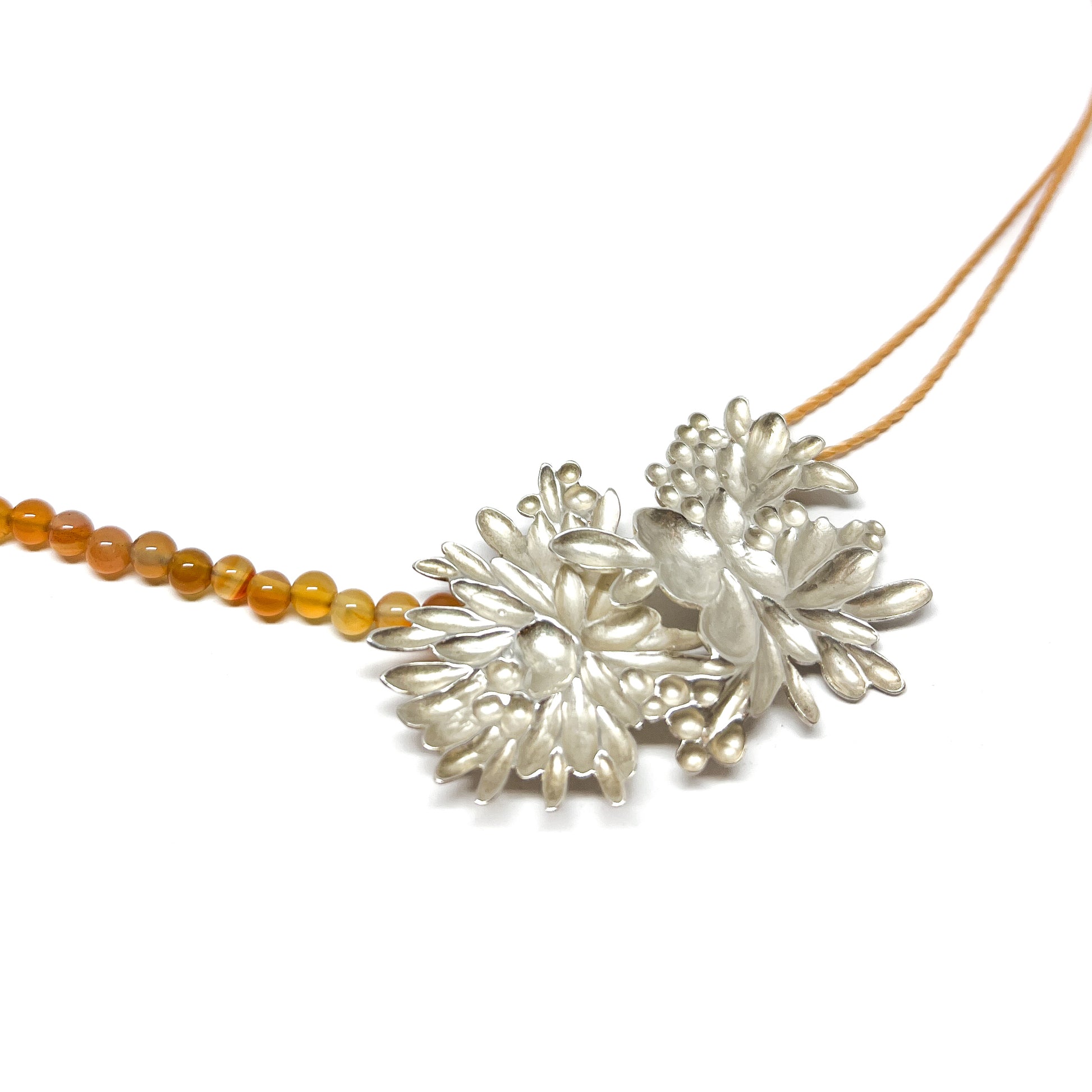 Close-up of a necklace with a large, textured silver floral pendant and a strand of small, round orange beads.