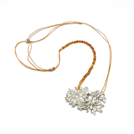 A necklace featuring a large, textured silver floral pendant attached to a strand of small, round orange beads and a thin cord.