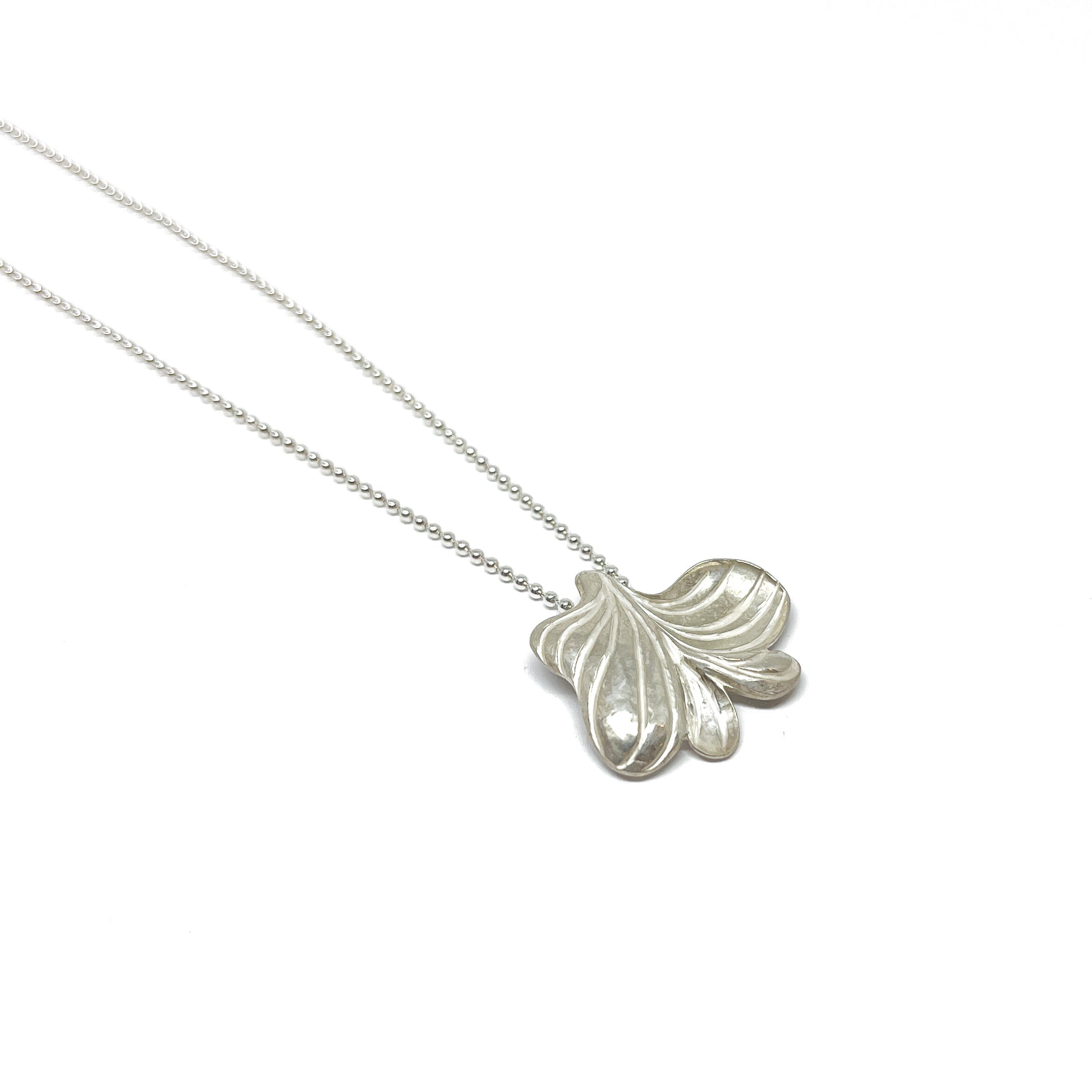A silver necklace with a textured, abstract pendant resembling stylized leaves or petals on a delicate beaded chain.