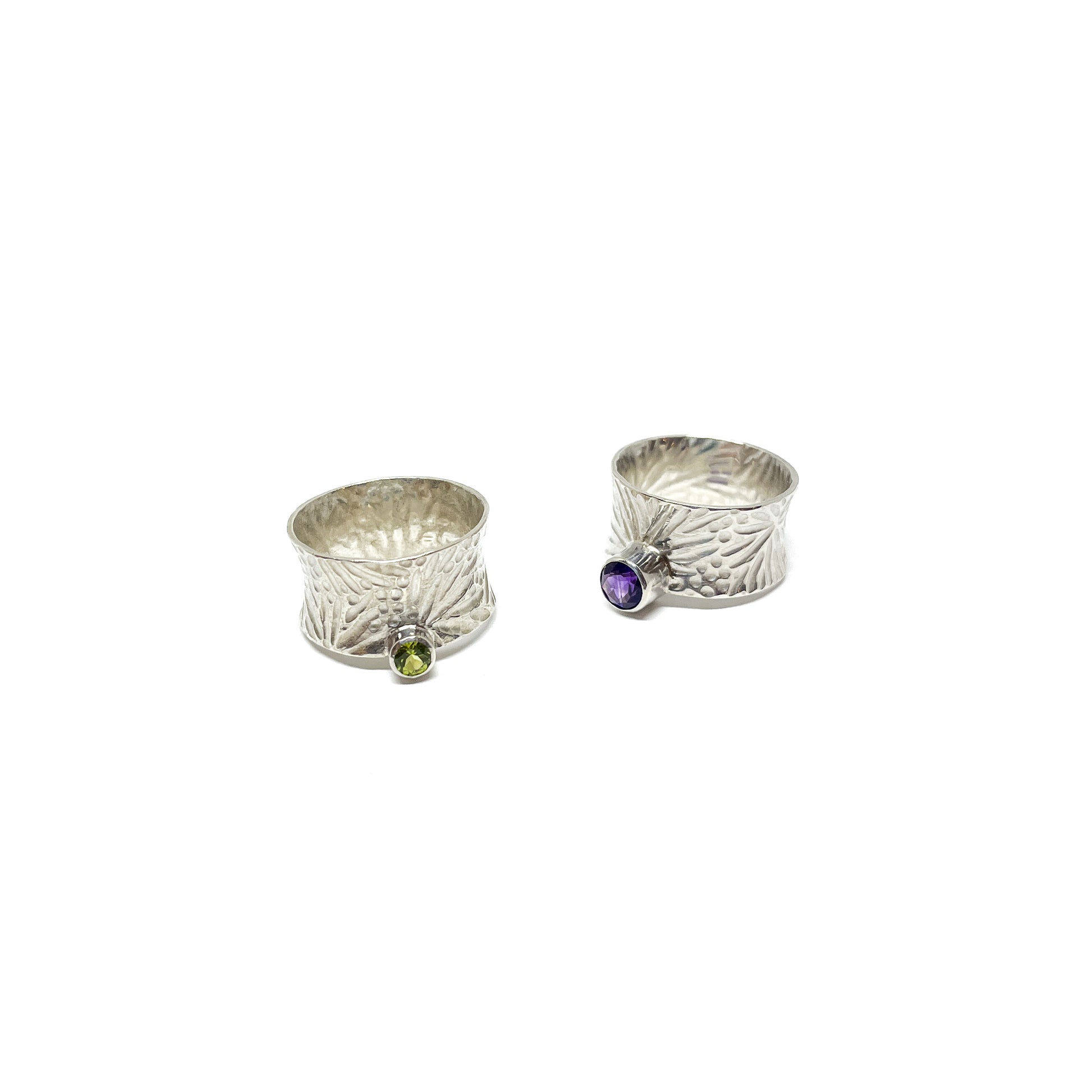 Two textured sterling silver spinner rings. One features a peridot, the other an amethyst gemstone.