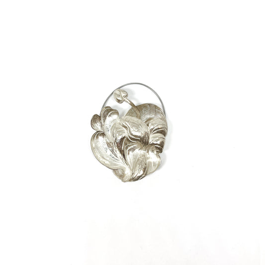 A silver brooch featuring a textured, abstract floral or lily-like design with curved, overlapping elements.