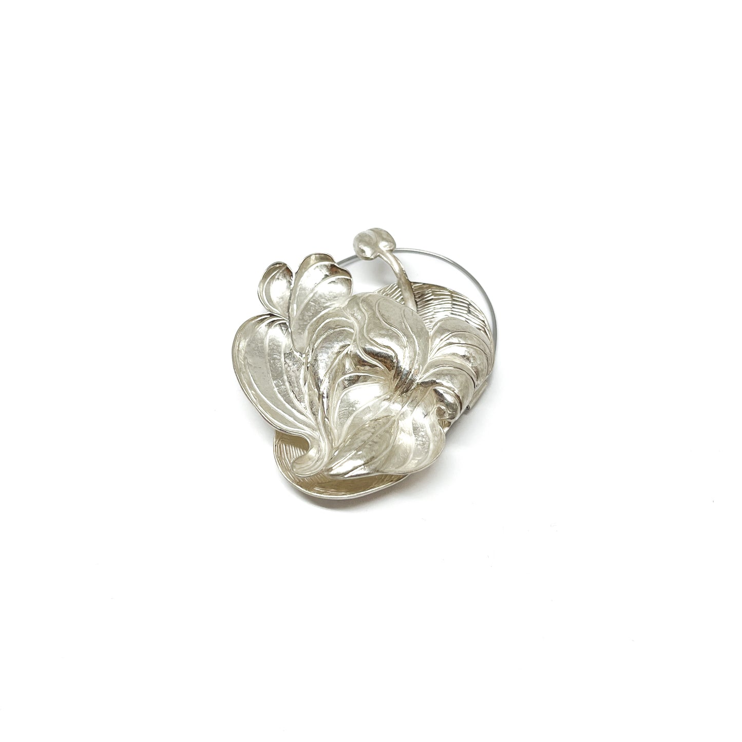 A silver brooch in the shape of a textured, stylized wildflower or lily with flowing, curved petals and a stem.