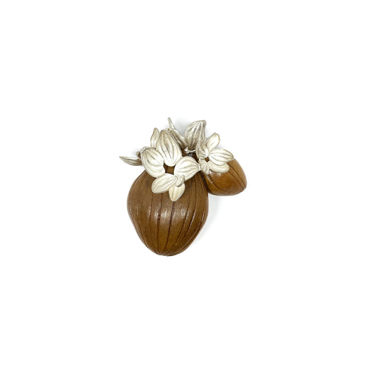 A textured silver brooch featuring stylized leaves and buds emerging from two smooth, brown seed-like forms.
