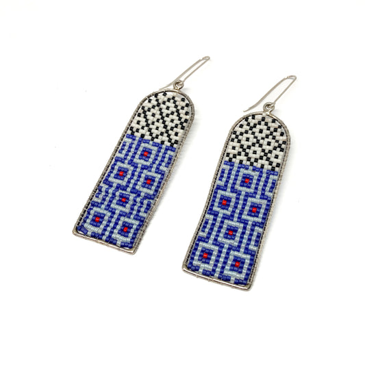 Two long, arched dangle earrings feature intricate beadwork in white, black, blue, and red within silver frames.