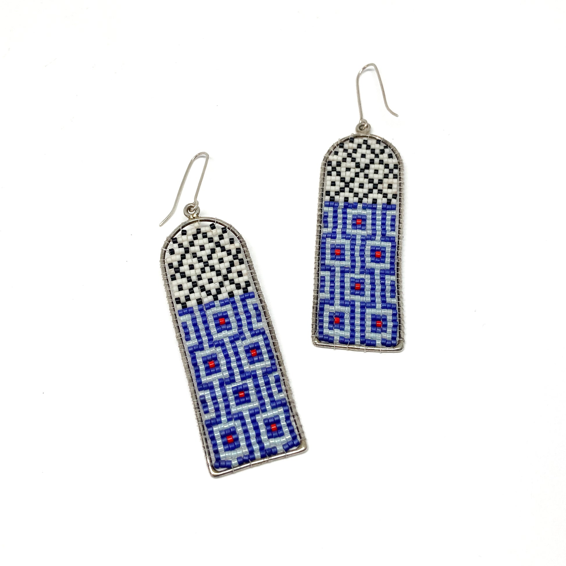 Two long, arched dangle earrings feature intricate beadwork in white, black, blue, and red within silver frames.