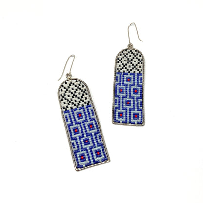 Two long, arched dangle earrings feature intricate beadwork in white, black, blue, and red within silver frames.