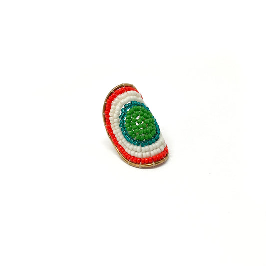 A gold ring features concentric circles of green, teal, white, and red beads forming a vibrant, textured design.