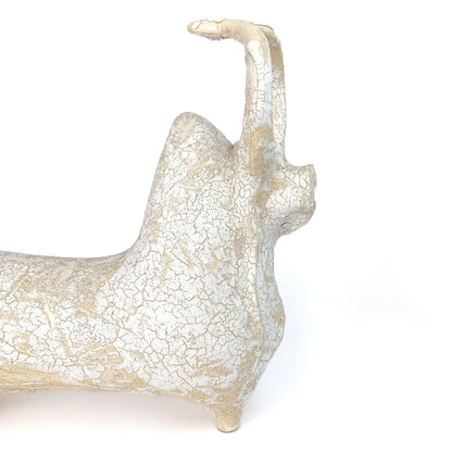 A textured, light-toned ceramic bull figurine with its head and tail raised, featuring a distinct crackled glaze.