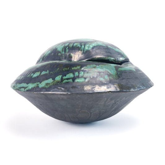 A dark, layered ceramic UFO vessel with a textured surface and drips of teal glaze.