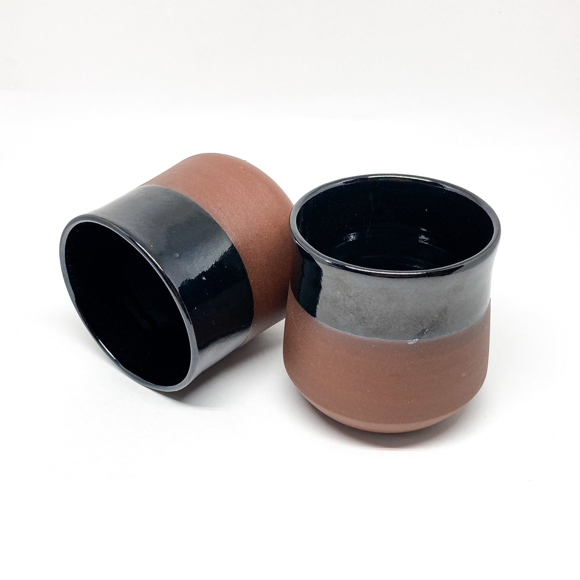 Two two-toned wine cups with brown bases and black rims, one lying on its side.