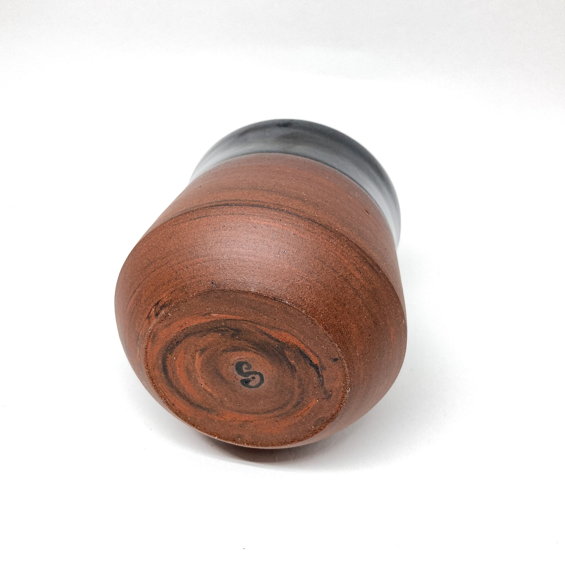 Bottom view of a two-toned wine cup with a brown base and black rim, showing a letter "S" on the base.