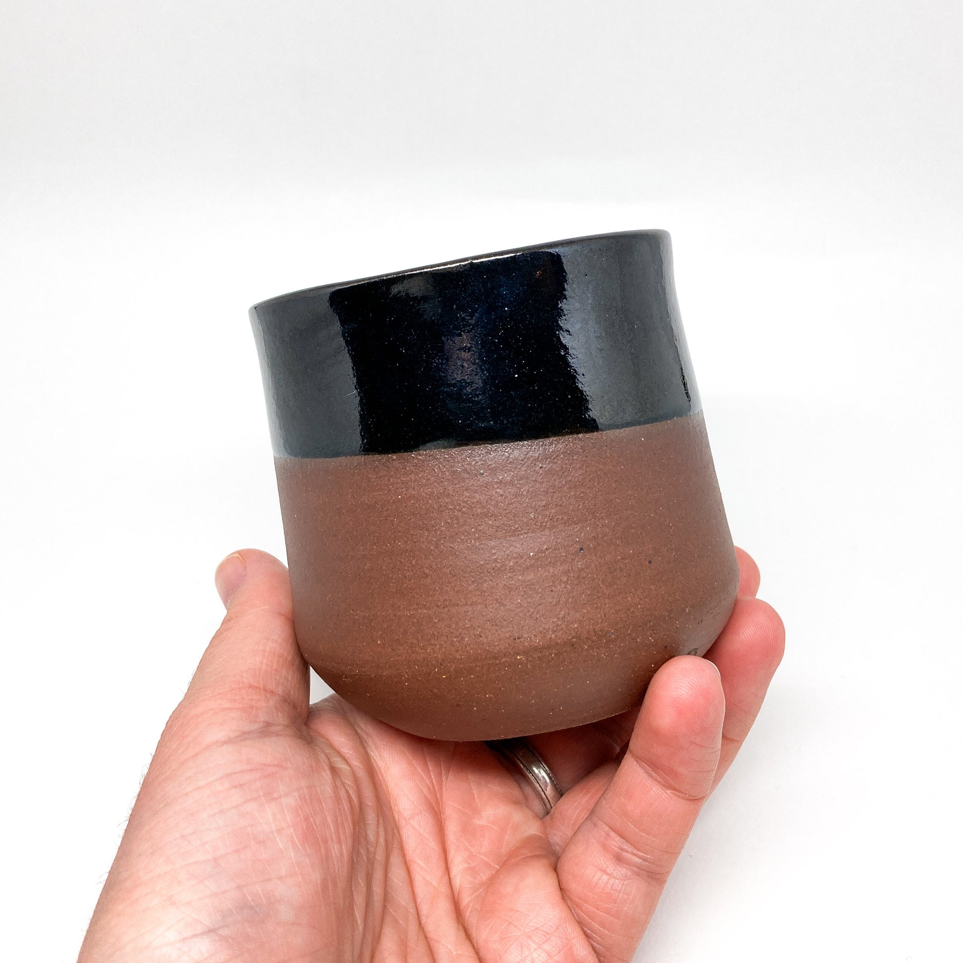 A hand holding a two-toned wine cup with a brown base and black rim.
