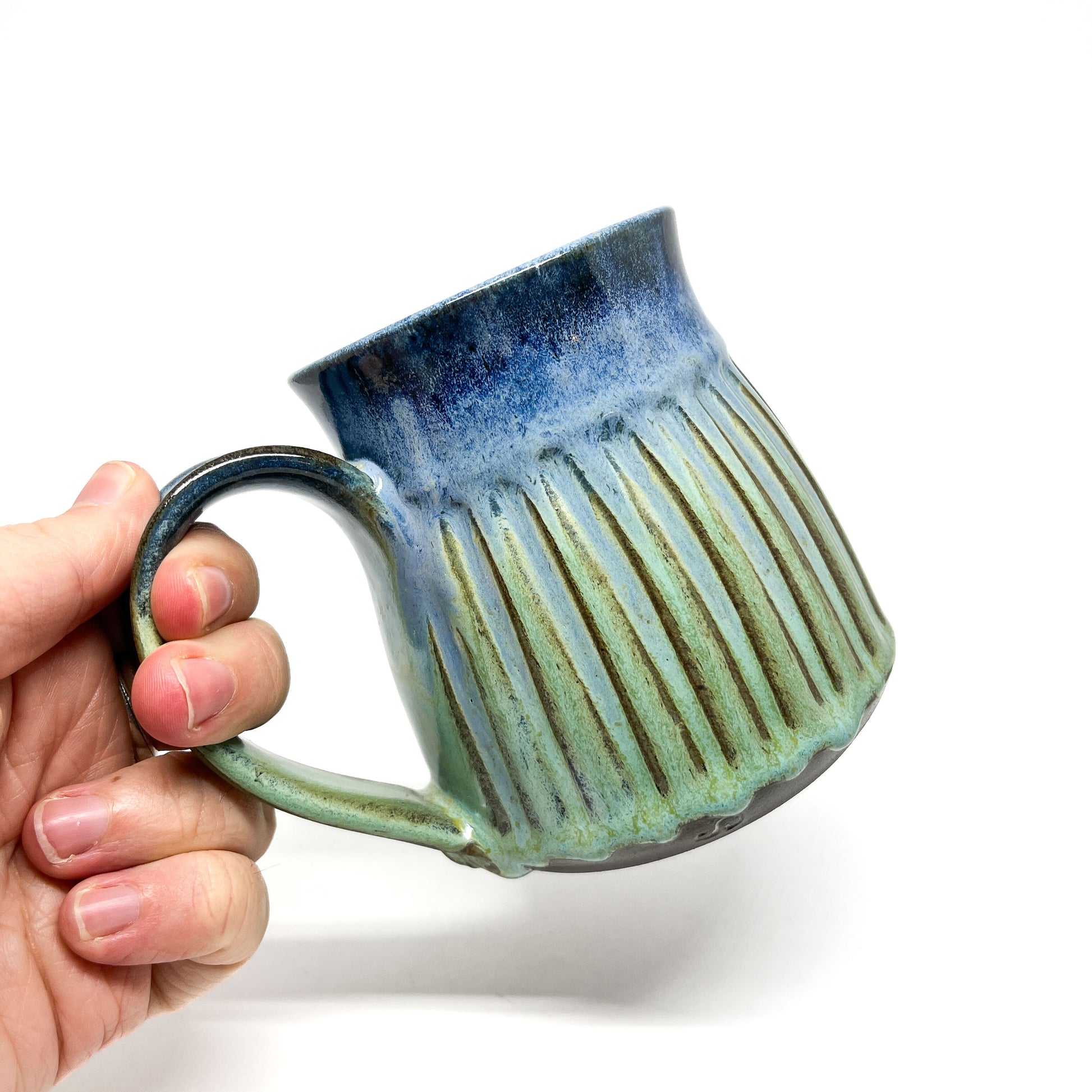 A hand holding a ceramic mug with a ridged texture and a blue-to-green gradient.