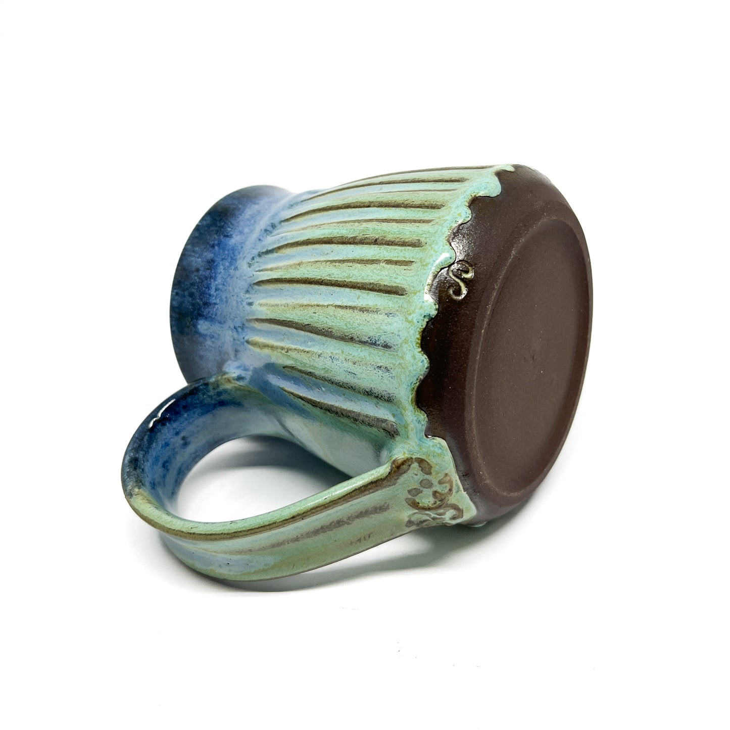 A close-up of the bottom of a ceramic mug with a ridged texture, featuring a blue-to-green gradient and a small inscription.