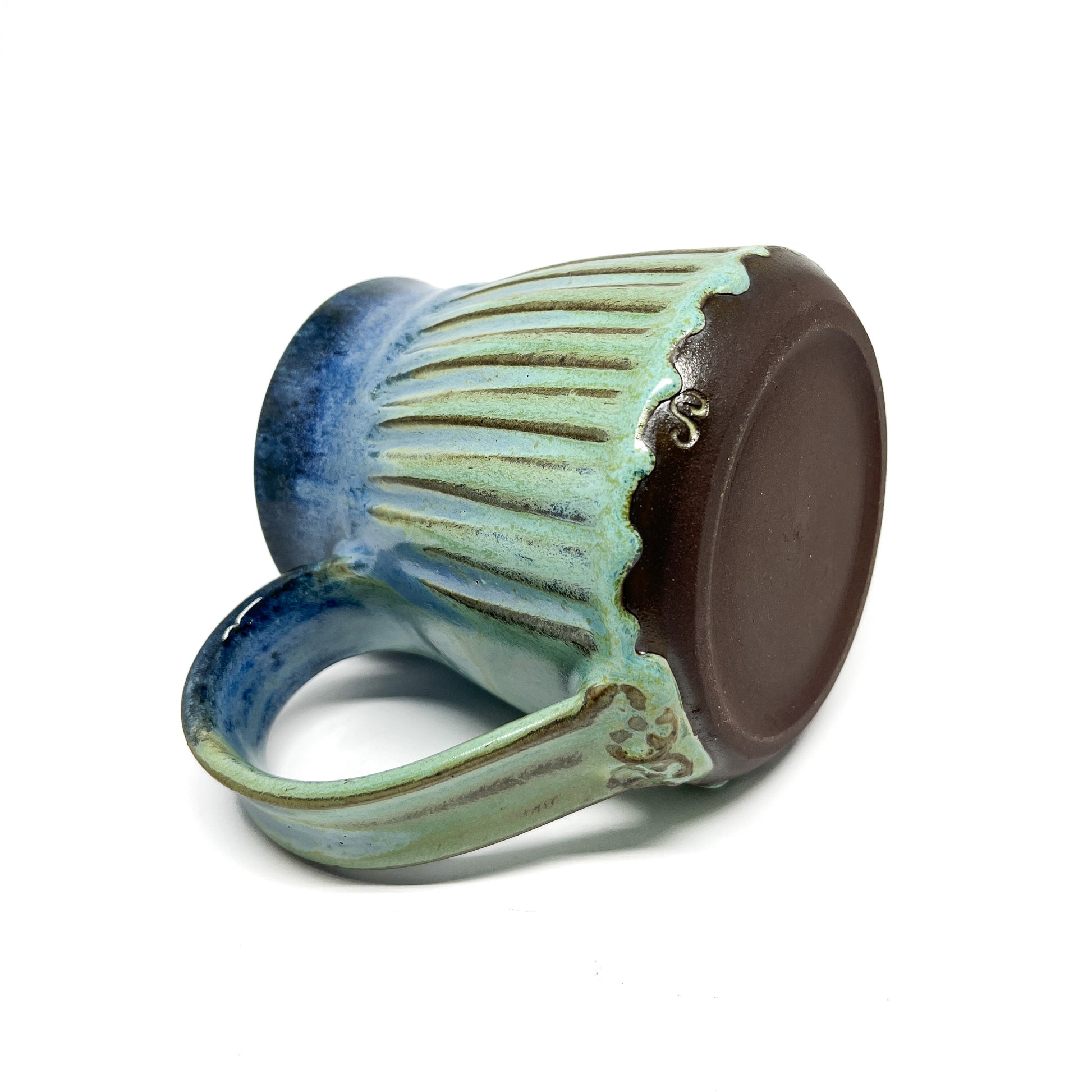A close-up of the bottom of a ceramic mug with a ridged texture, featuring a blue-to-green gradient and a small inscription.
