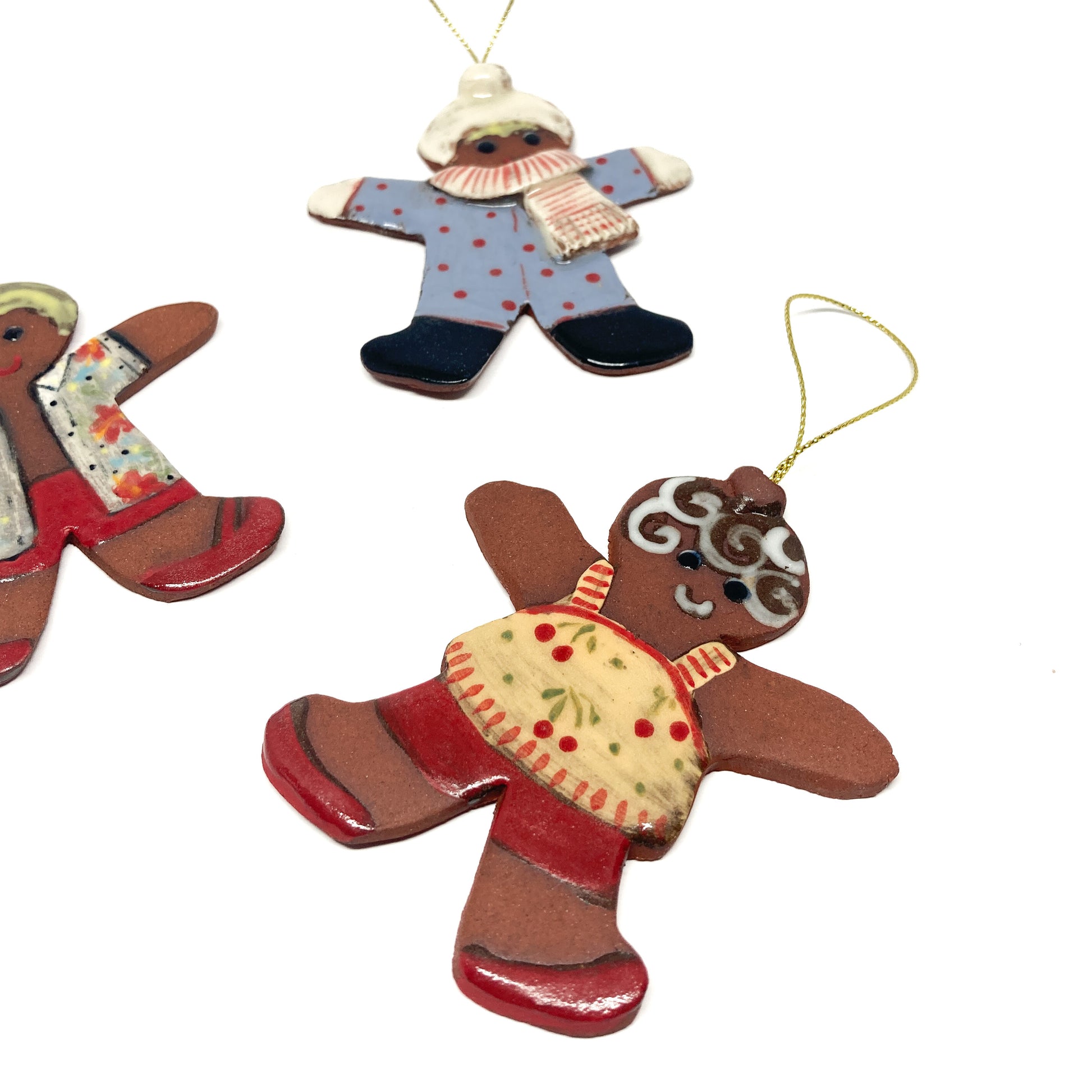Three gingerbread ornaments with different outfits and gold strings.