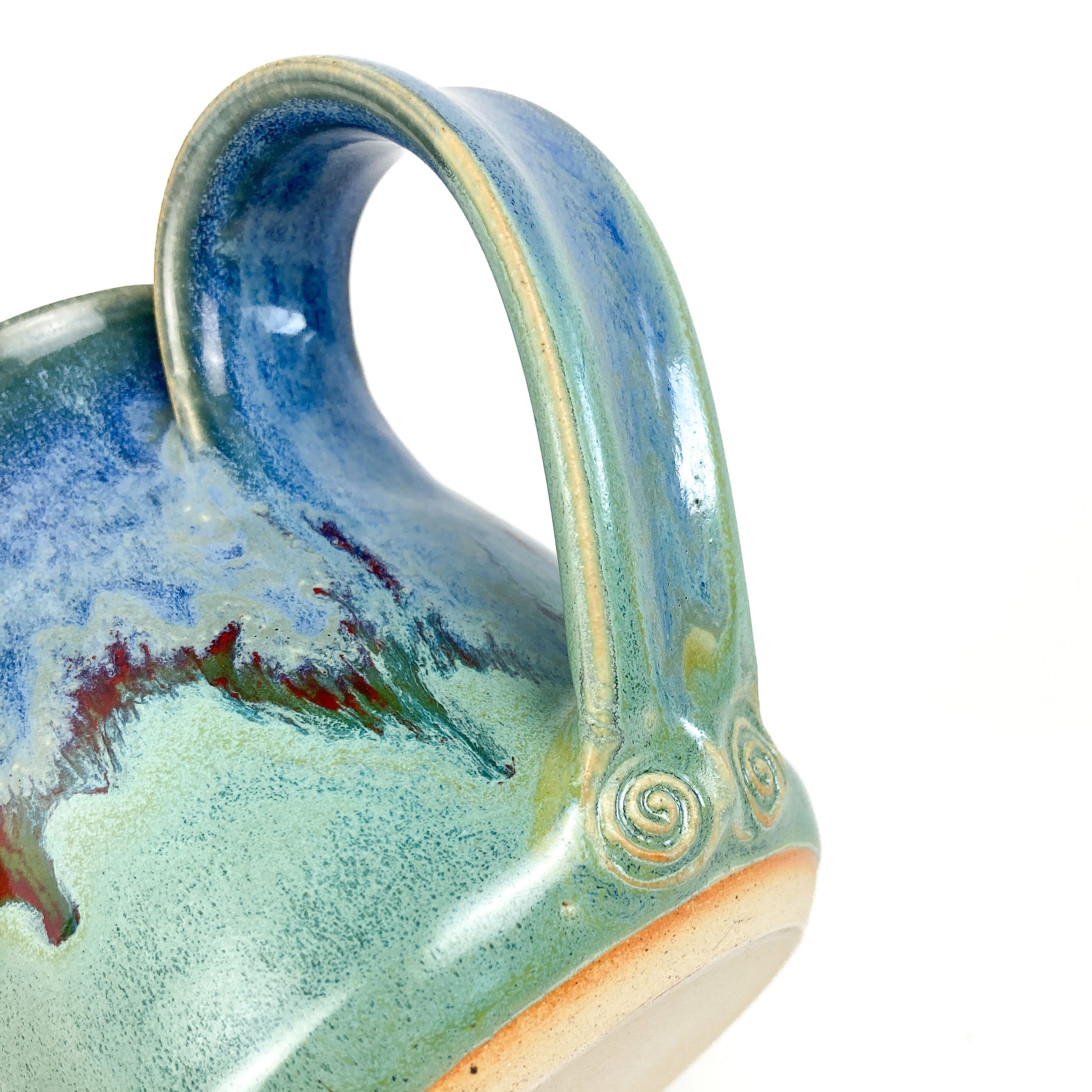 A close-up of a ceramic mug handle with a blue-to-green gradient and red accents, showing a spiral detail.