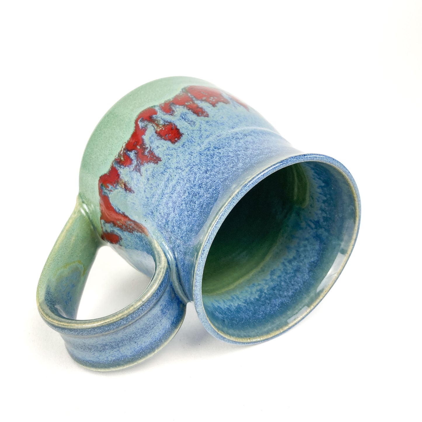A ceramic mug with a blue-to-green gradient and red accents, tilted on its side.