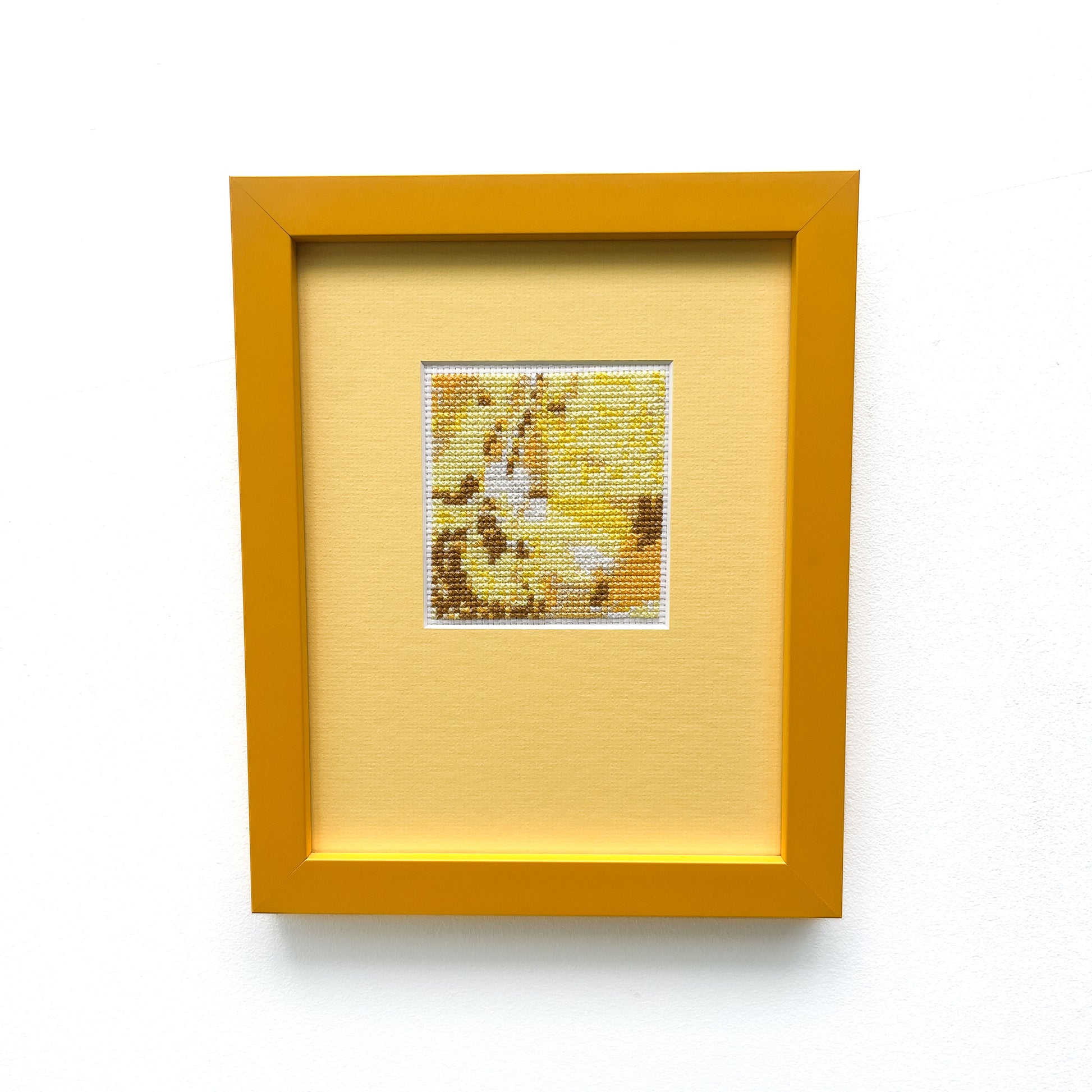 Framed "Yellow Monochrome" cross-stitch. A small square of stitched art is centered on a larger yellow mat within a yellow frame.