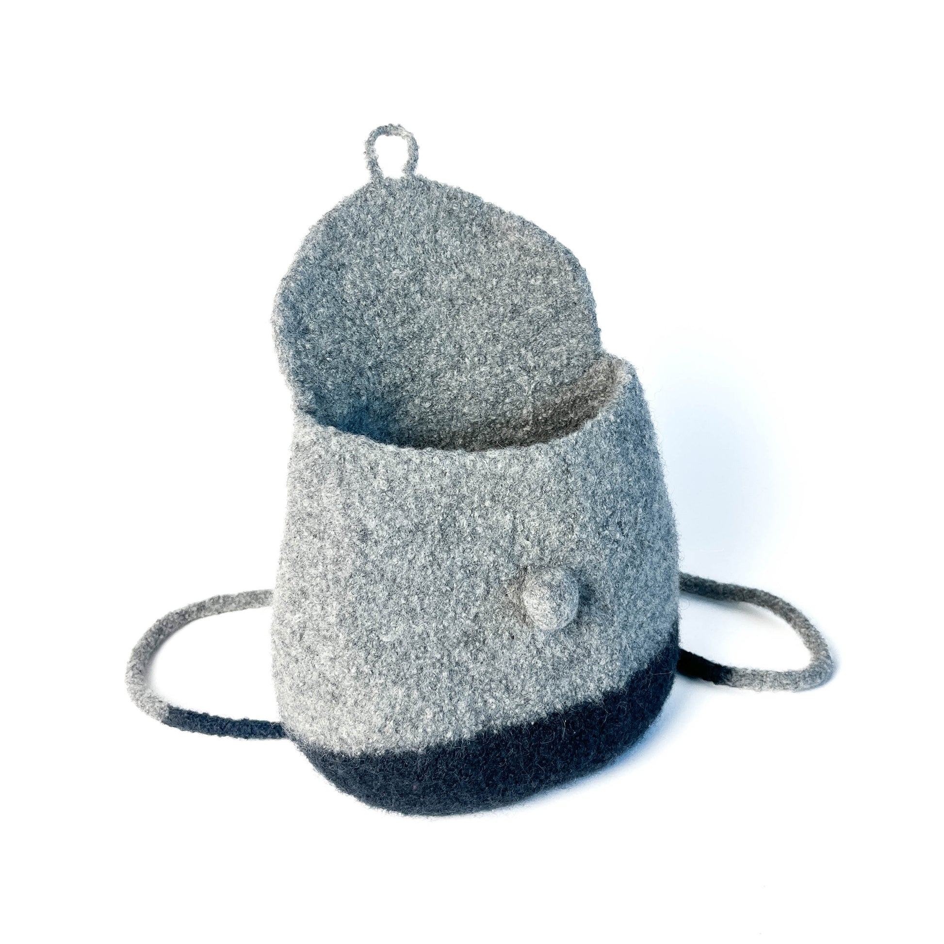 Two-tone felted backpack with an open flap closure, button detail, and thin shoulder straps.