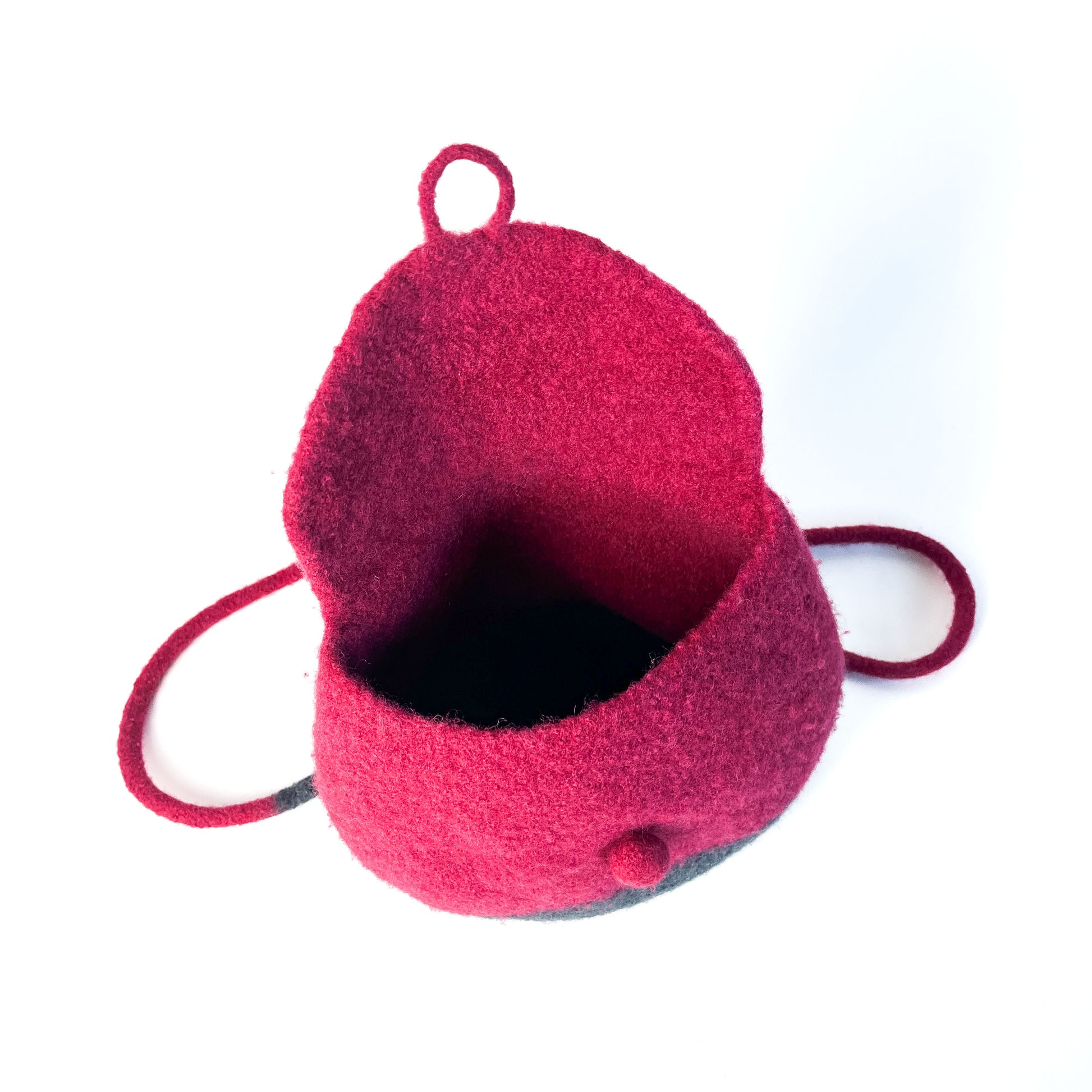Open, two-tone felted backpack with a button detail and thin shoulder straps, showing the dark interior. The upper portion is a vibrant color.